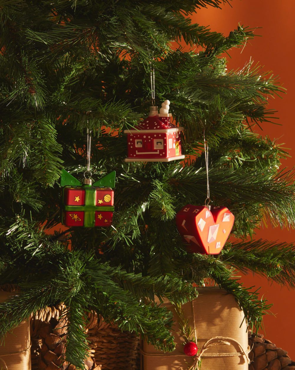 Red, green, and white Christmas tree ornaments by Alessi, including a house, gift box, and geometric heart with patterns.