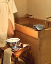 Three-wick Rocc candle by Alessi in a polished silver bowl, lit, with bath salts and a comb.