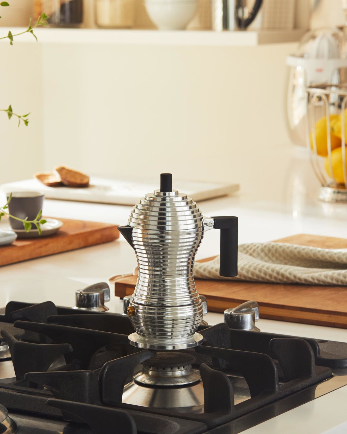 Silver ribbed espresso coffee maker by Alessi, with a black handle, on a gas stove in a bright kitchen.