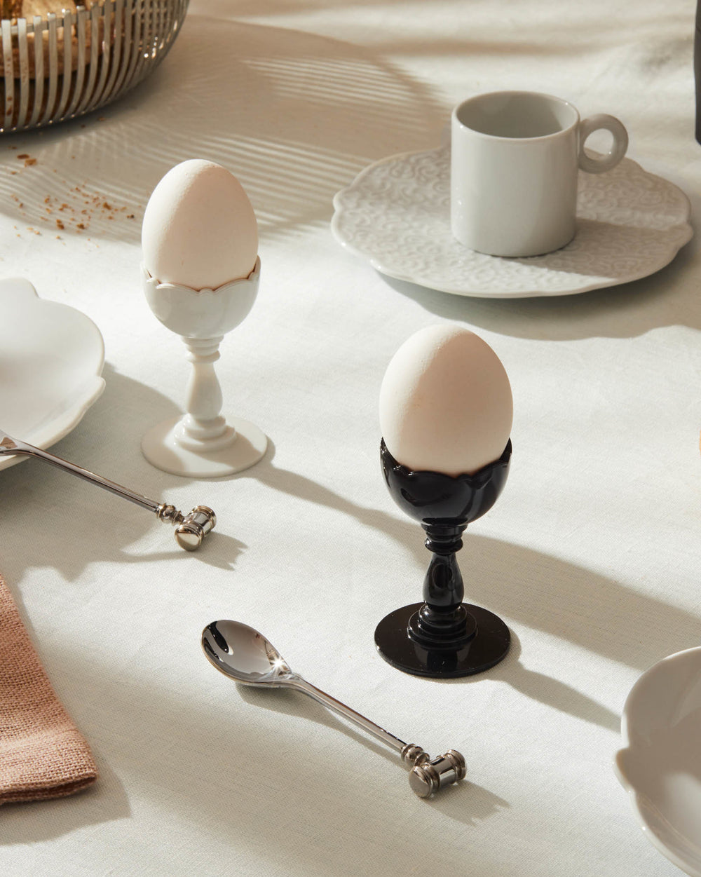 Two Dressed egg cups by Alessi, one white ceramic and one black ceramic, with scalloped rims and pedestal bases.