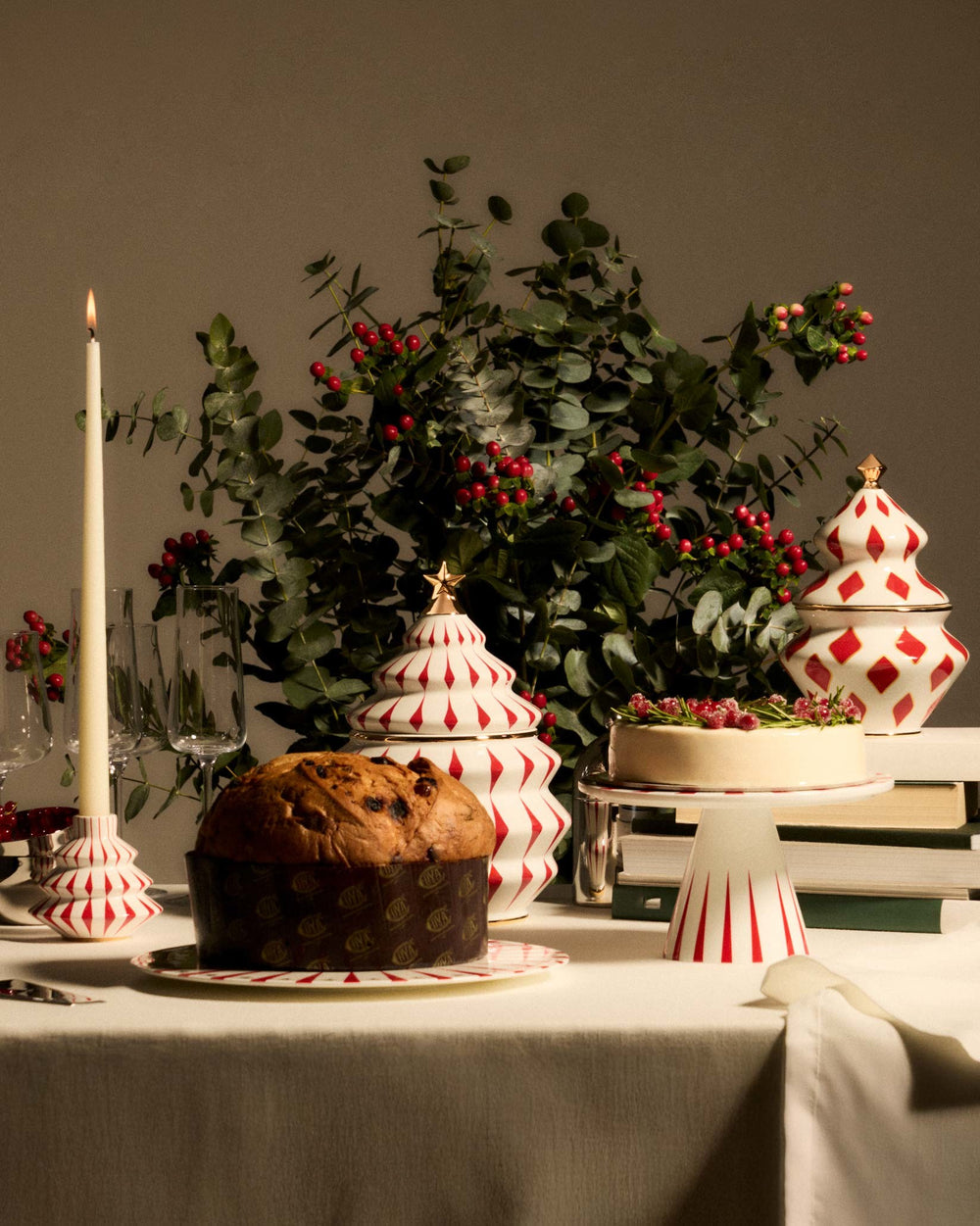 White ceramic Christmas tree-shaped centerpiece by Alessi, with red diamond patterns and a gold star on top, on a festive table.
