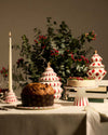 White tree-shaped decorative jars by Alessi, adorned with red diamond patterns and gold star finials, on a festive table.