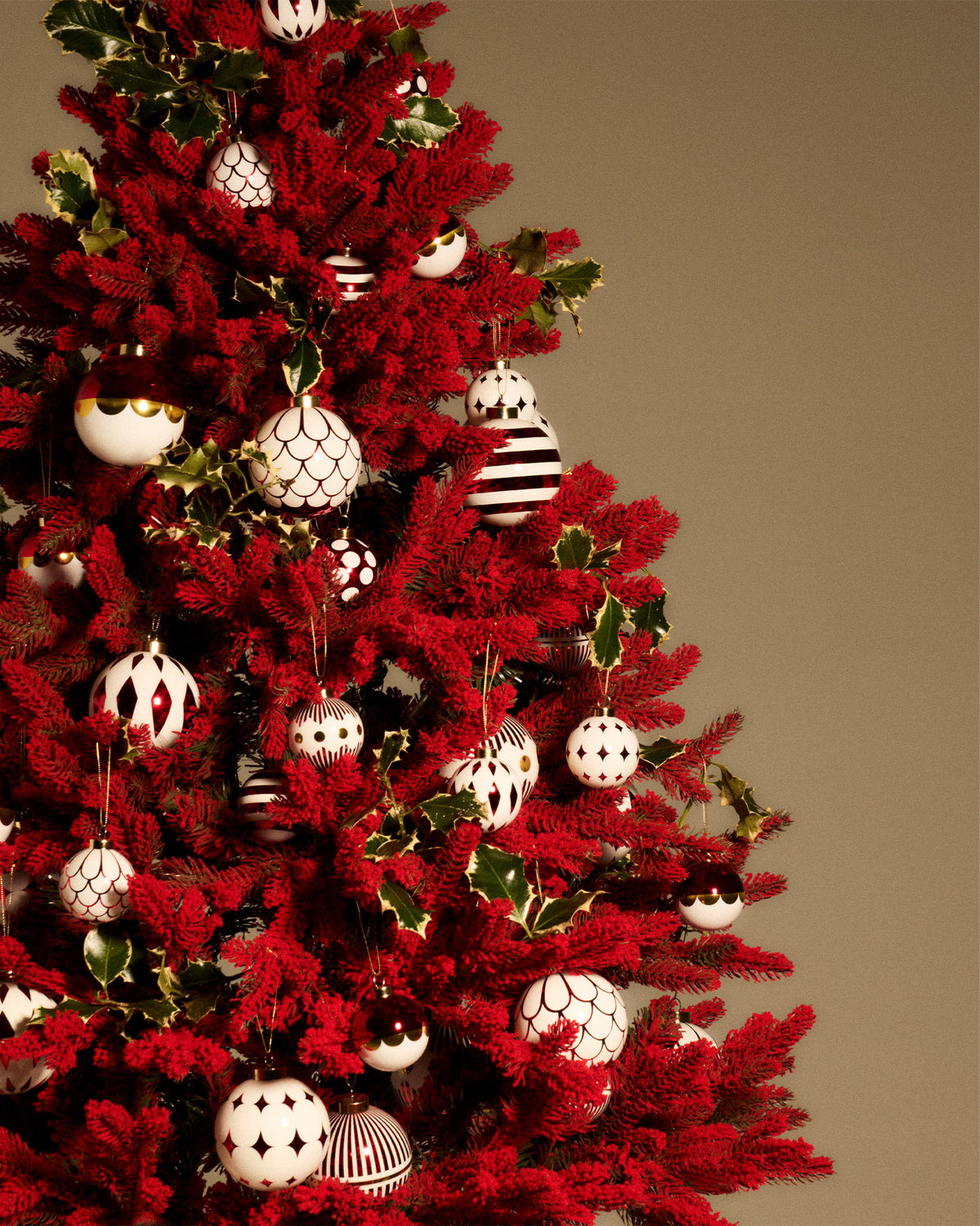 White and red patterned Christmas tree ornaments by Alessi on a vibrant red flocked tree with holly.
