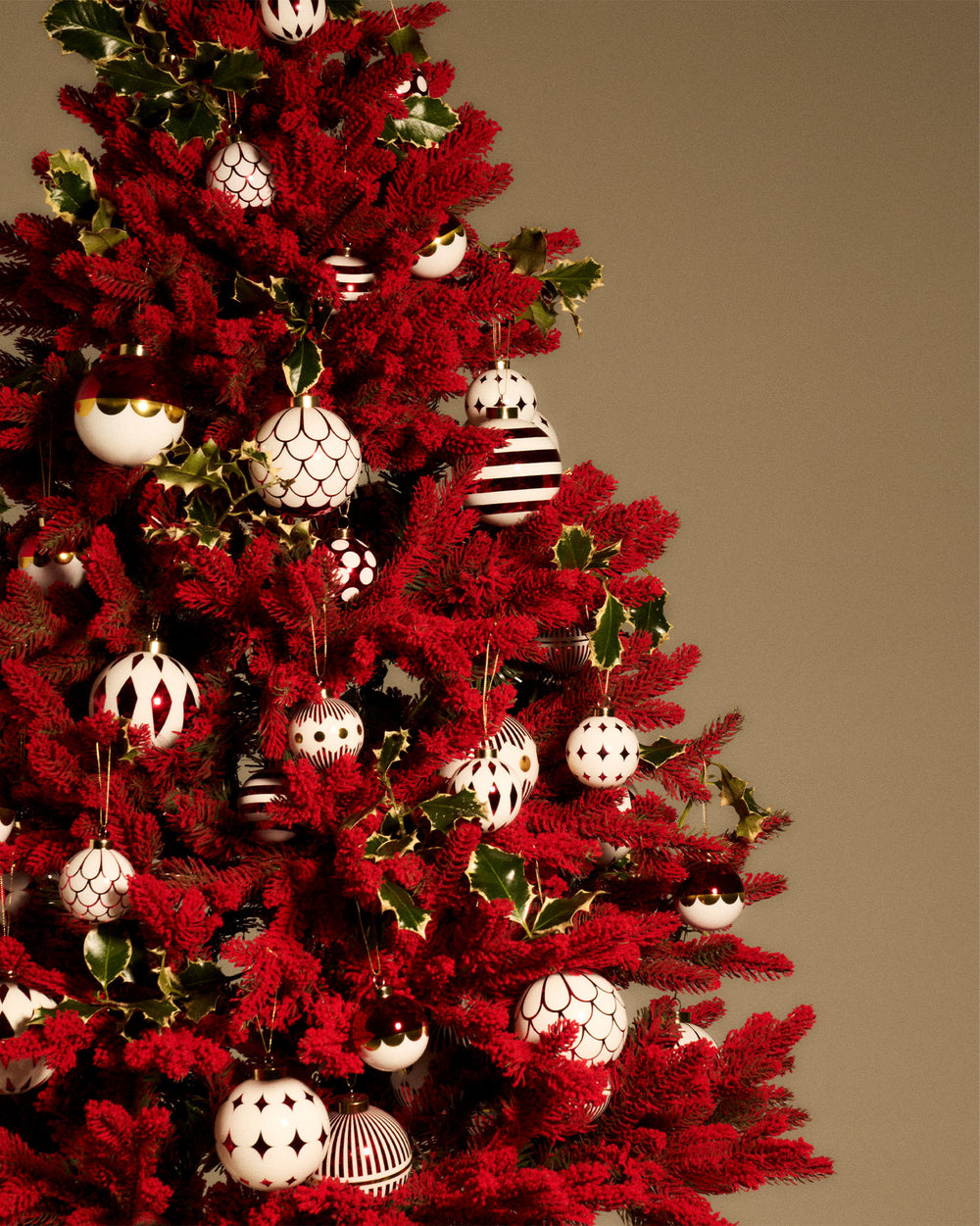 White, red, and gold Christmas tree ornaments by Alessi featuring varied patterns including stripes, dots, scales, and diamonds on a red Christmas tree.