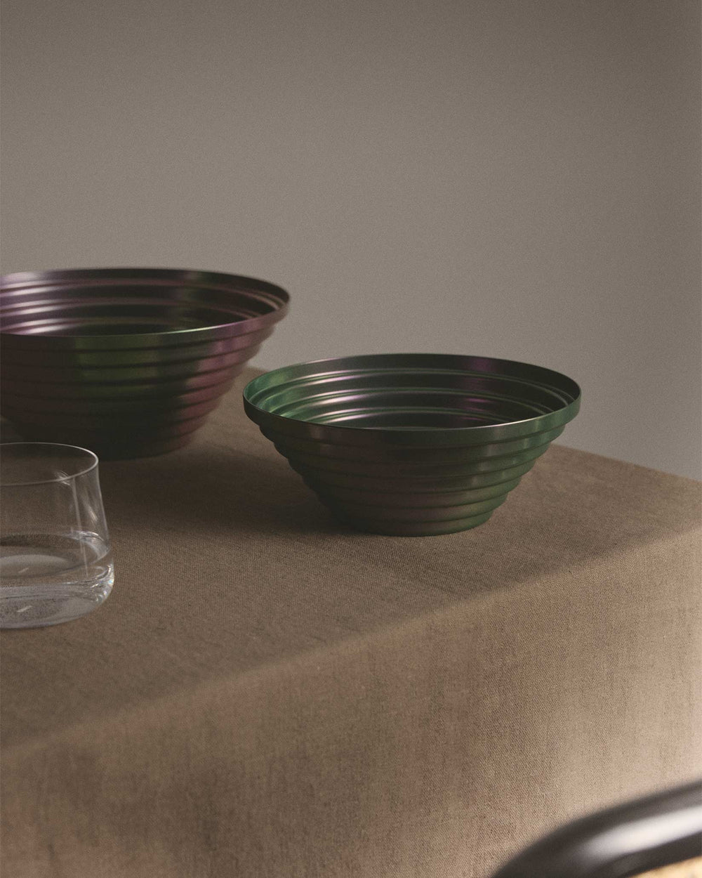 Iridescent fluted metal bowls by Alessi, two sizes, on a brown tablecloth.
