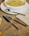 Polished silver Clivo table spoon by Alessi, featuring a sleek flat handle, on a white plate.