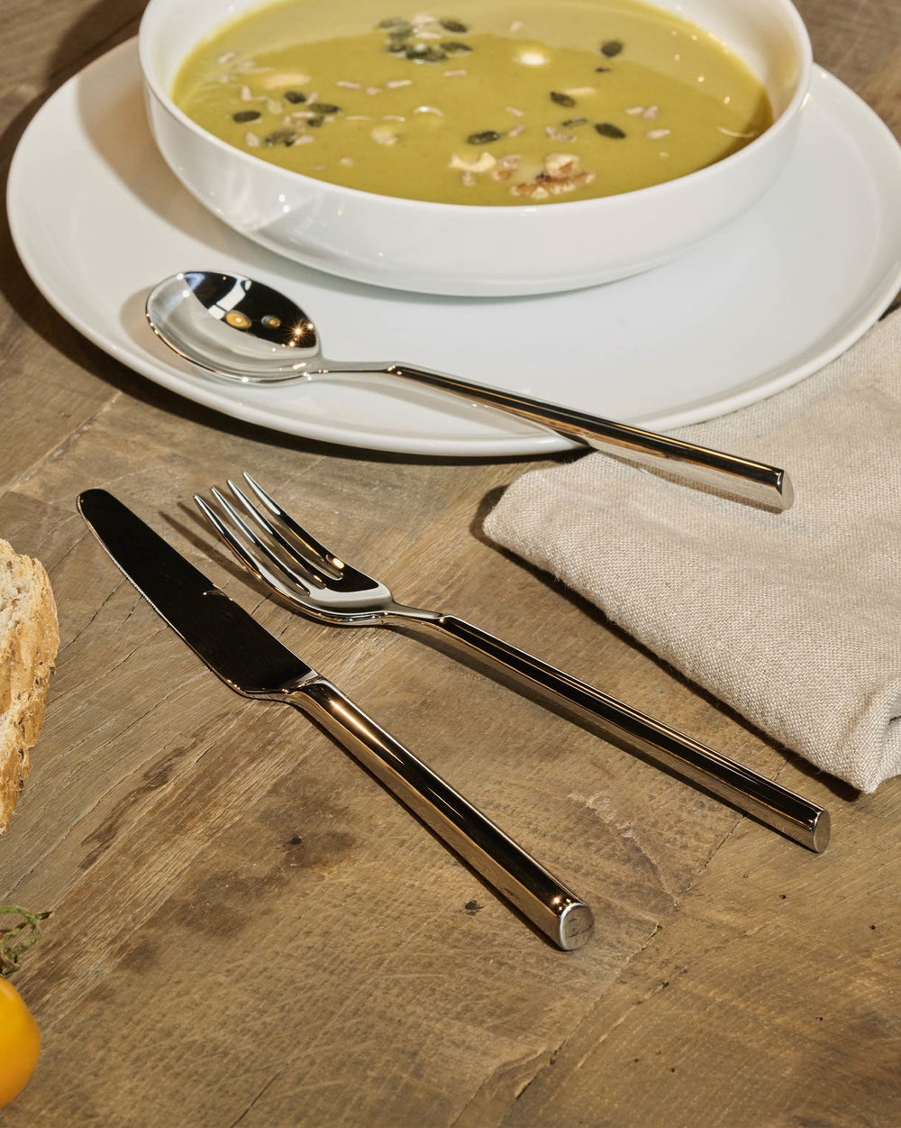 Sleek polished silver flatware set by Alessi, with rectangular handles, on a white plate.