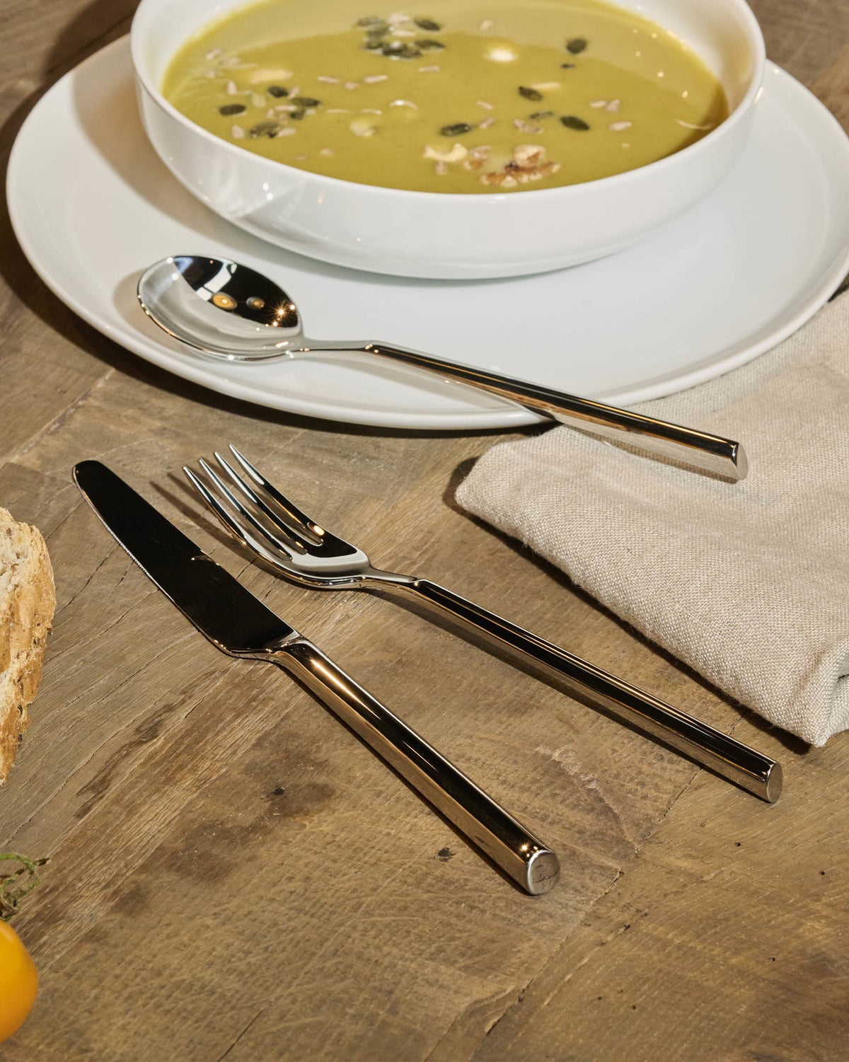 Clivo polished silver-tone metal table knife by Alessi, featuring a sleek, rectangular handle, resting on a rustic wooden table.