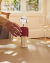 Figural corkscrew with chrome head, red shirt, and cream pants by Alessi, a woman's hand reaching for it on a table with wine glasses.