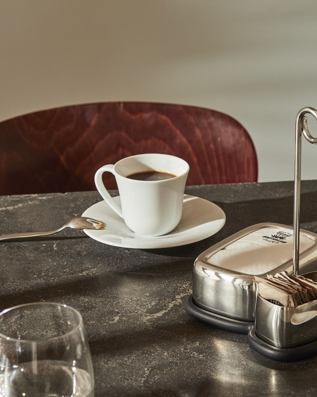 White ceramic espresso cup by Alessi with a curved handle and saucer, styled on a dark table.