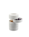 White vertically pleated capsule holder by Alessi, with a rotating tier revealing gold and purple coffee capsules.