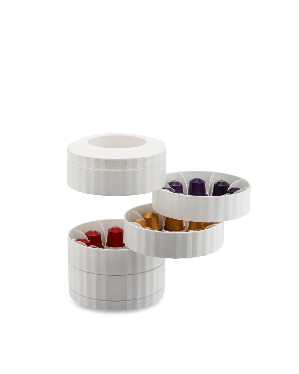 White fluted capsule holder by Alessi, with three tiered sections holding colorful red, gold, and purple coffee capsules.