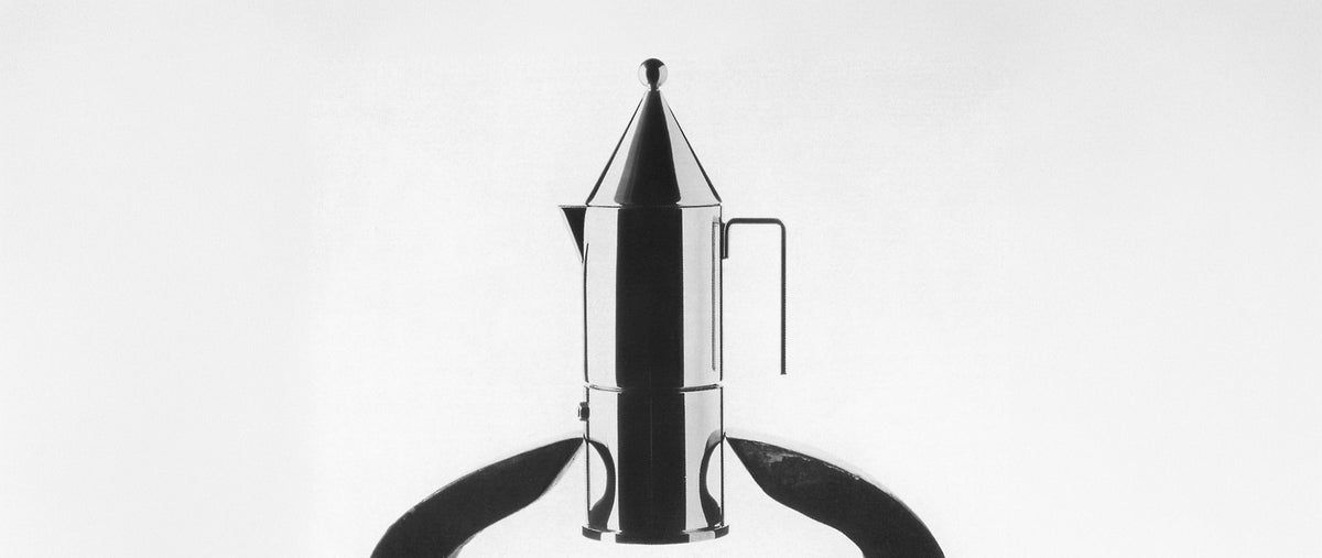 Shiny chrome coffee percolator with conical lid and curved handle, centered on white background.