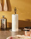 Polished chrome paper towel holder with an abstract coral-shaped top by Alessi, holding a white paper towel roll on a counter.