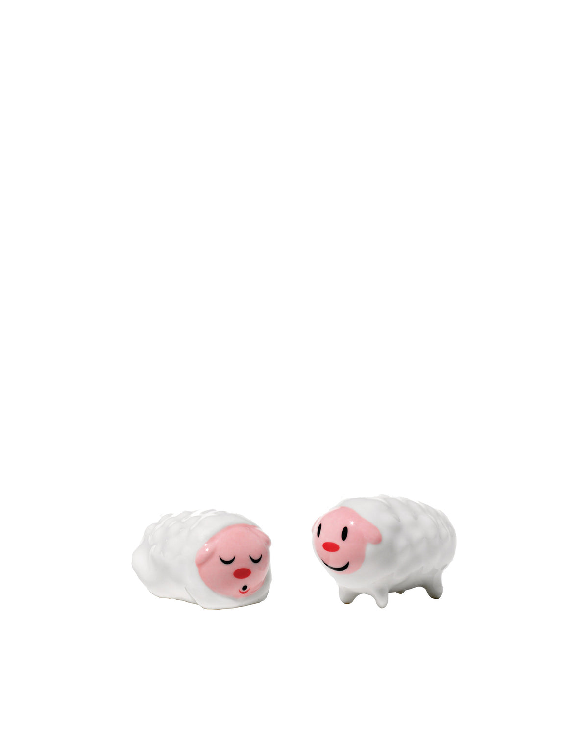 White ceramic sheep figurines by Alessi, one sleeping and one smiling, with rosy faces and textured bodies.