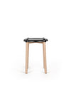 Black-seated stool by Alessi with a distinctive wavy seat and natural light wooden legs on a white background.