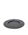 Round matte dark grey trivet by Alessi with a central well and seven smaller circular indentations.