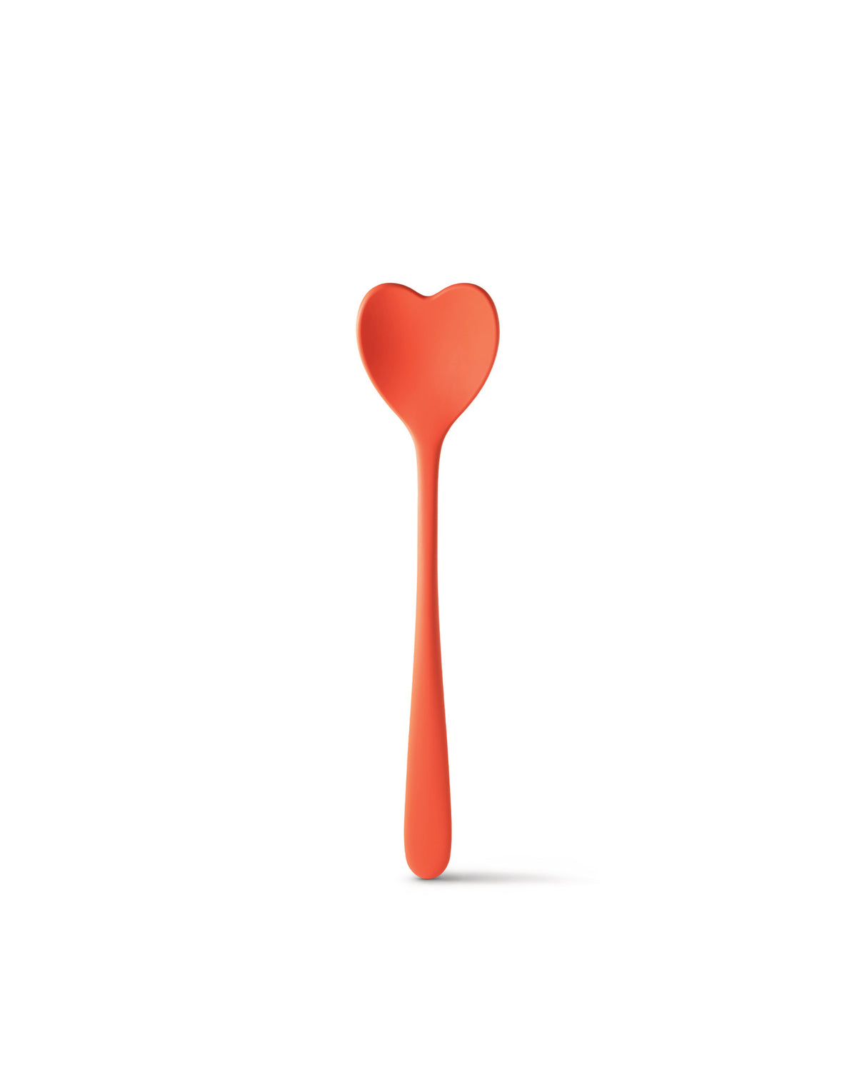 Large coral heart-shaped spoon by Alessi with a long handle, standing upright and casting a soft shadow.