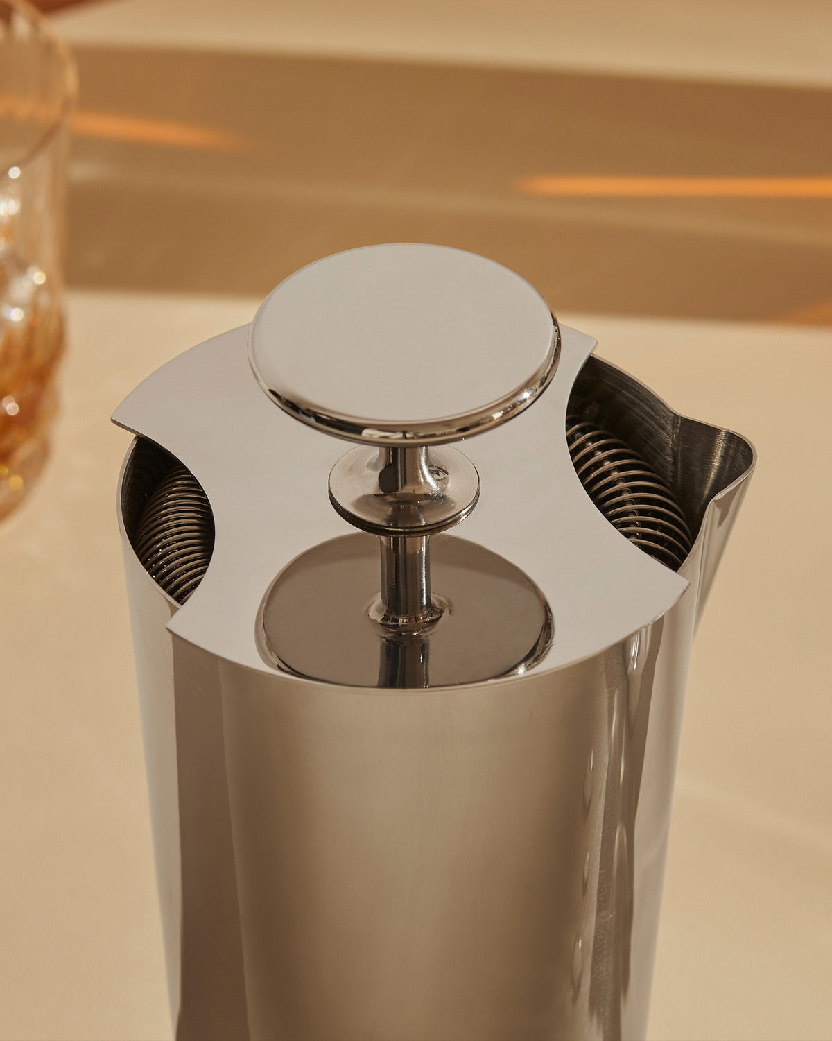 Silver metallic tending box by Alessi with a circular lid and three openings revealing internal coils, seen from above.
