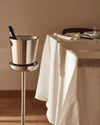 Stainless steel champagne cooler and stand by Alessi, holding a bottle next to a set dining table.