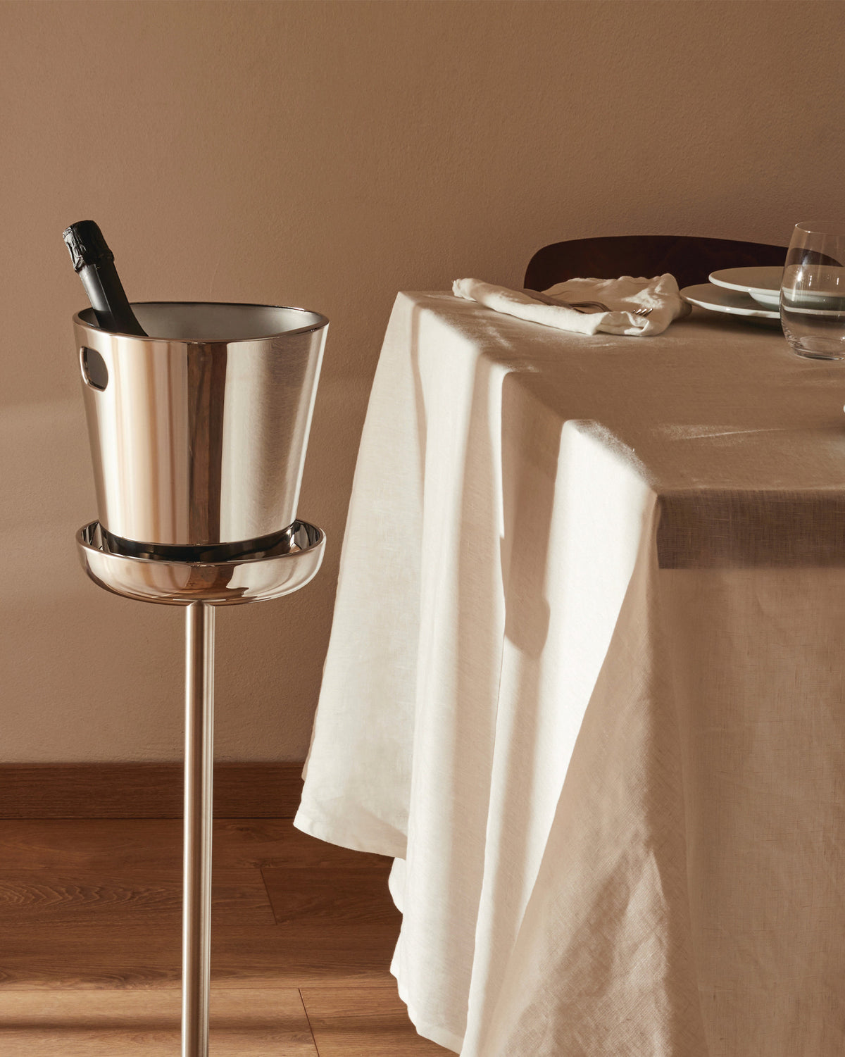 Stainless steel champagne cooler and stand by Alessi, holding a bottle next to a set dining table.