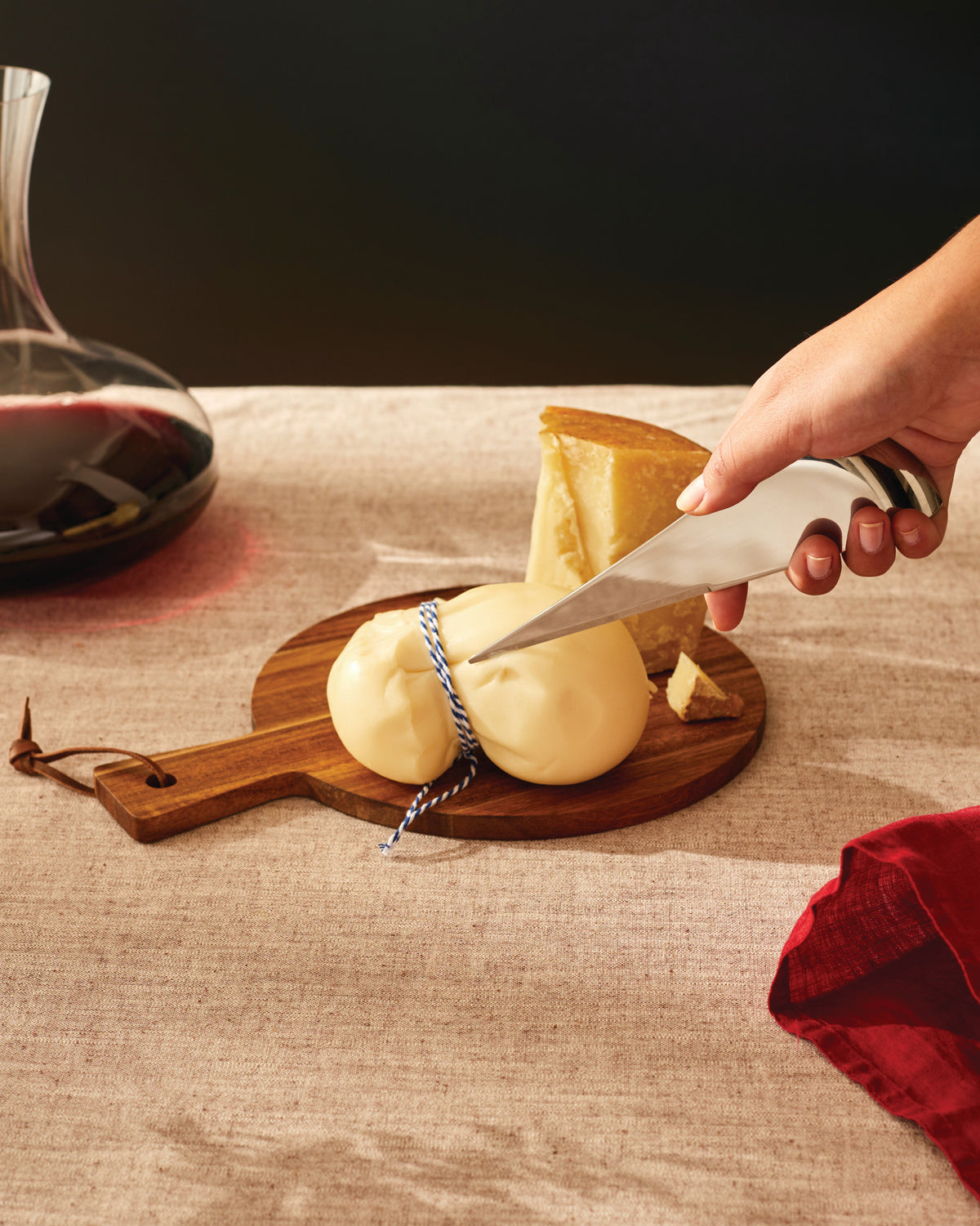 Silver Antechinus cheese knife by Alessi, cutting into soft yellow cheese on a wooden board.