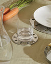 Round silver metal coaster with Girotondo cut-out figures by Alessi, holding a glass of water on a green tablecloth.