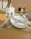 Silver metal coral-shaped napkin holder by Alessi, holding white paper napkins on a green tablecloth.