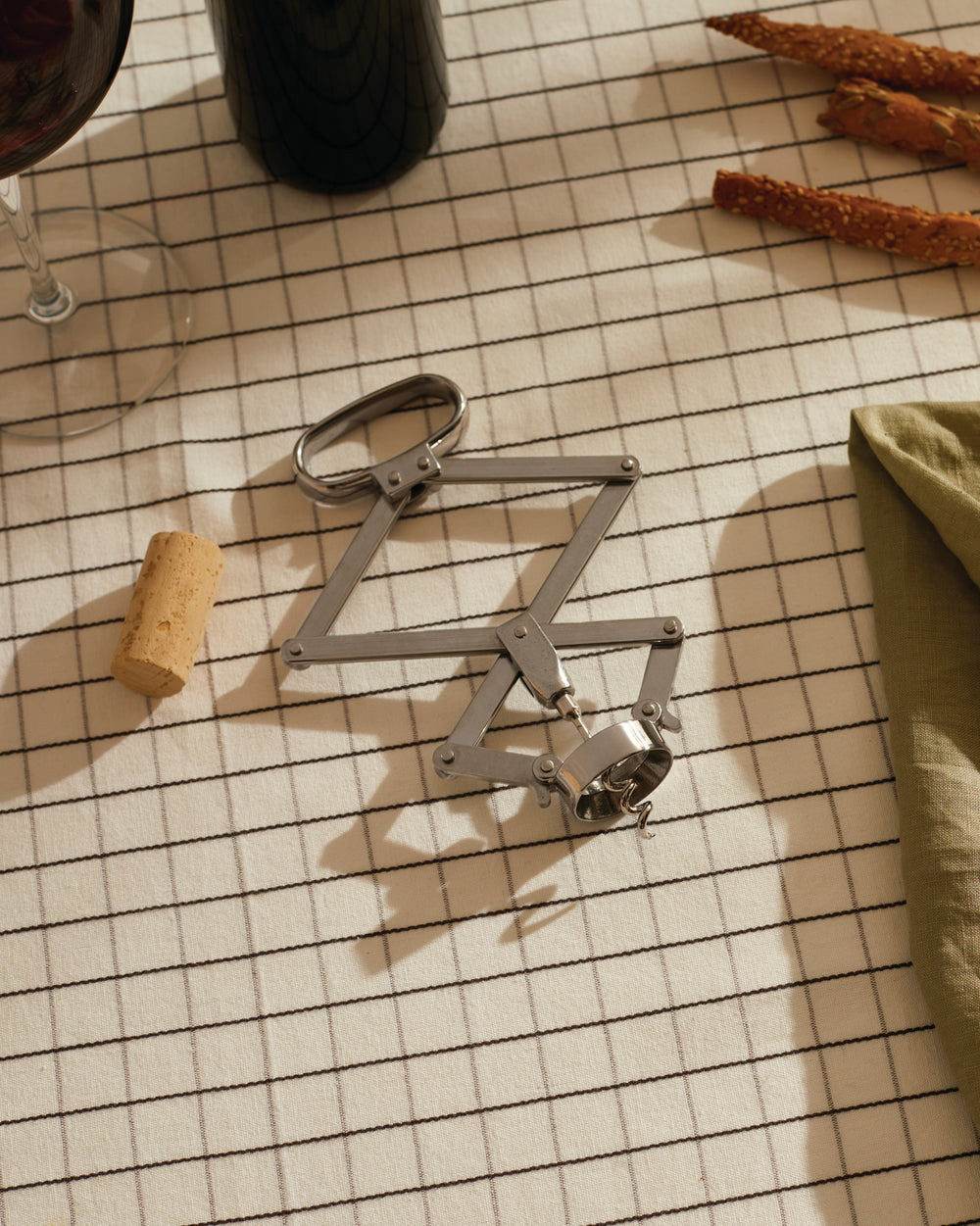 Metallic Socrates corkscrew by Alessi with a folding geometric design on a plaid tablecloth.