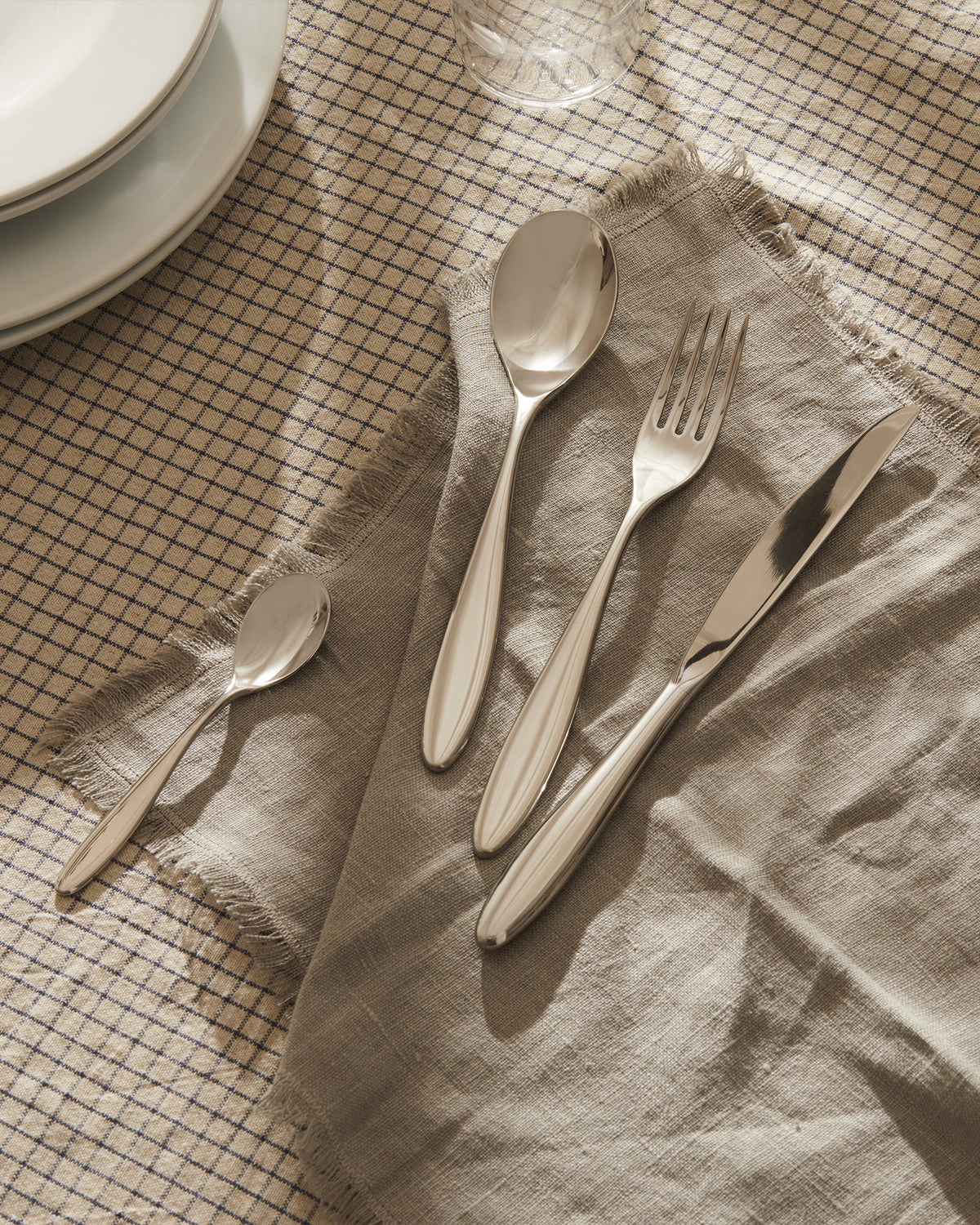 Sleek silver cutlery by Alessi, including a spoon, fork, and knife, resting on a frayed linen napkin.