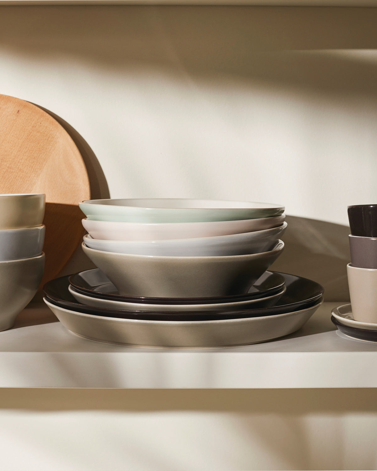 Assorted ceramic bowls and plates by Alessi in various neutral and pastel tones, neatly stacked on a shelf.