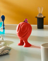 Red Gino Zucchino dispenser by Alessi, designed with a smiling face and purple pour spout, on a counter.