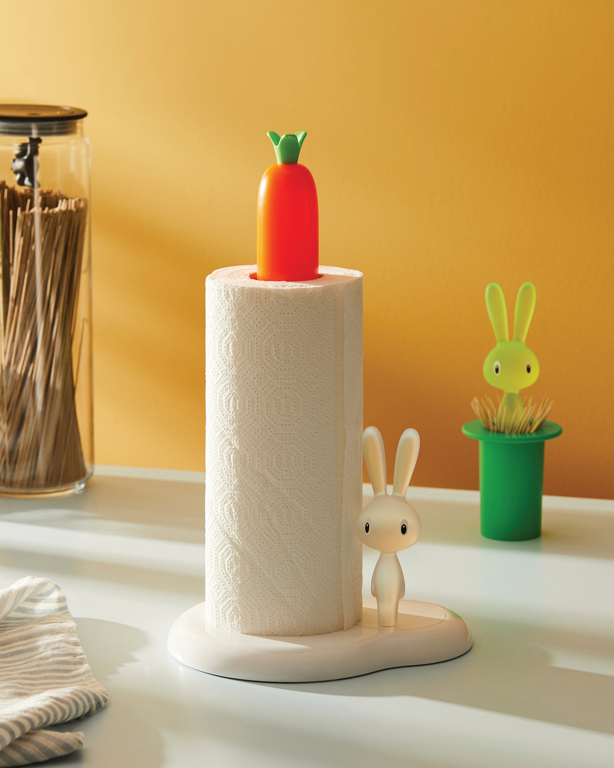 White Bunny & Carrot paper towel holder by Alessi, with an orange carrot finial and a white bunny figurine, on a countertop.