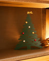 Green metal Christmas tree decoration by Alessi, featuring a golden shooting star and colorful baubles, displayed in a fireplace.