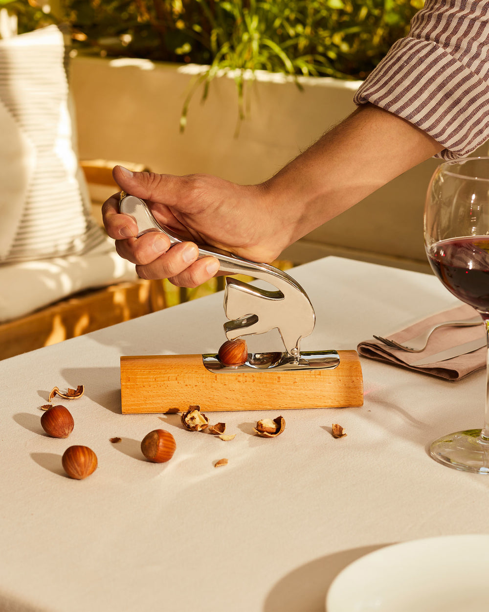 Polished metal and wood squirrel-shaped nutcracker by Alessi, shown cracking a hazelnut on a light tablecloth.