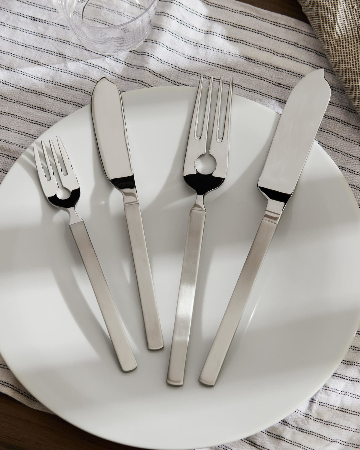 Silver fish cutlery set by Alessi on a white plate with a striped napkin.