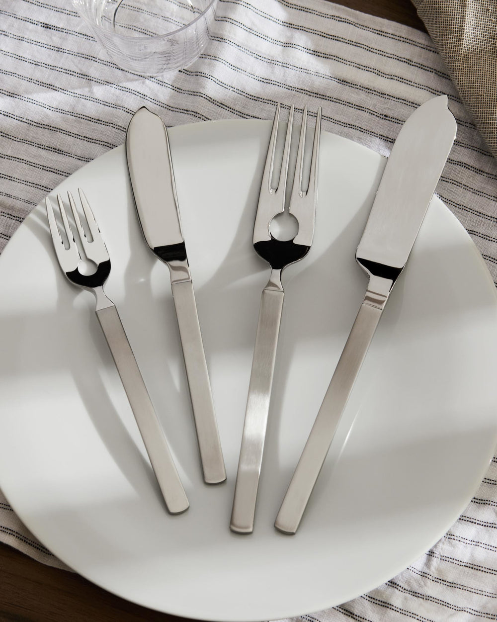Silver-toned stainless steel four-piece cutlery set by Alessi, with matte handles and polished heads, including a slotted fork, displayed on a white plate.