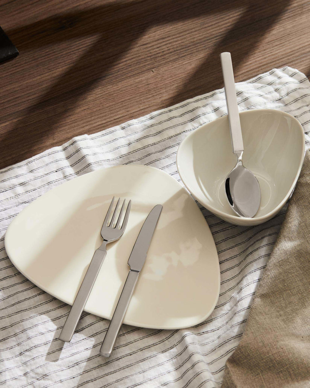 Silver stainless steel cutlery by Alessi on a striped napkin with cream dinnerware.