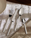 Sleek stainless steel cutlery set by Alessi, laid on a striped white napkin with a plate.