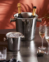 Dark metallic champagne cooler by Alessi, holding two bottles and covered in condensation, beside a smaller ice bucket and champagne flutes.