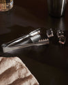 Stainless steel ice tongs by Alessi with serrated edges, next to ice cubes on a dark surface.