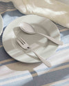 Sleek stainless steel spoon and fork by Alessi on a white plate and striped tablecloth.