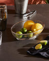 Silver metal oval wire fruit bowl by Alessi, holding lemons and limes on a dark counter.