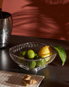 Silver wire fruit basket by Alessi, filled with limes and a lemon on a dark counter with ginger.