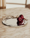 Silver polished tray with a wavy edge by Alessi, reflecting red apples on a marble surface.