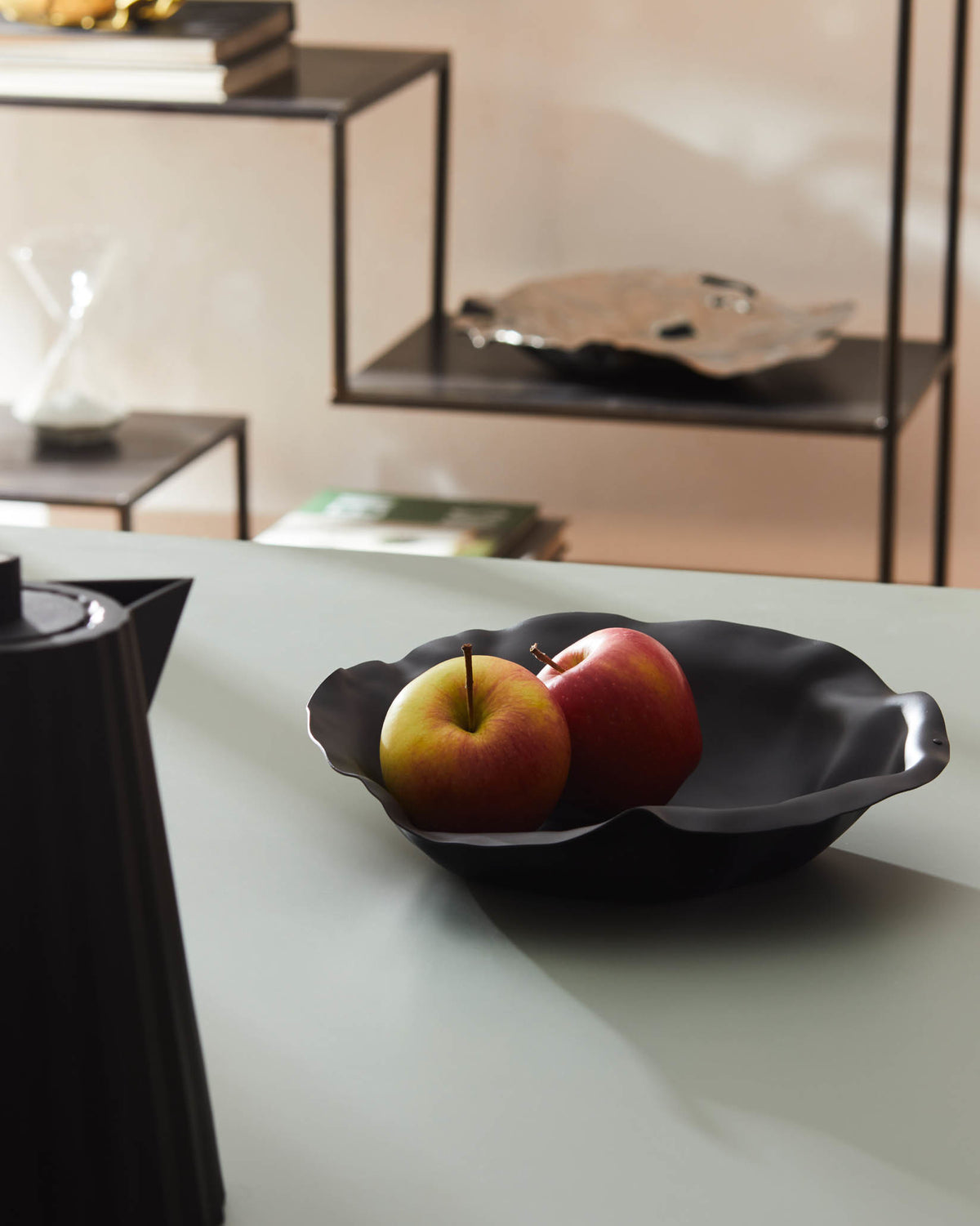 Black matte fruit bowl by Alessi with wavy edges, holding two apples on a light grey counter.