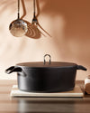 Black textured Dutch oven by Alessi with a flat lid and U-shaped handle, on a white marble trivet.