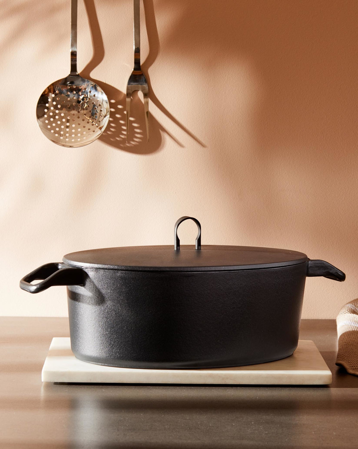 Black textured Dutch oven by Alessi with a flat lid and U-shaped handle, on a white marble trivet.