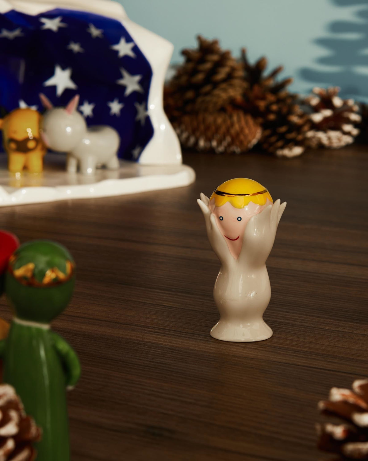 White ceramic Angelo Miracolo figurine by Alessi, with a yellow head and hands framing a smiling pink face.