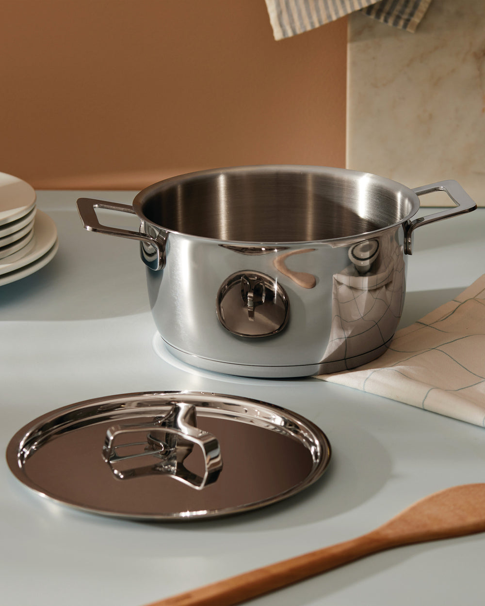 Stainless steel cooking pot by Alessi with a polished finish and its matching lid on a light countertop.